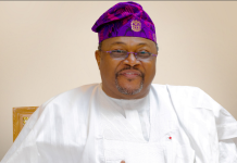 “A businessman with the Midas touch,” Tinubu hails Adenuga at 73 Smiling man wearing white traditional attire and a purple patterned cap, seated against a neutral background.