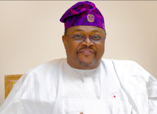 “A businessman with the Midas touch,” Tinubu hails Adenuga at 73 Smiling man wearing white traditional attire and a purple patterned cap, seated against a neutral background.