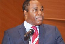 EFCC nabs ex-Skybank chair Tunde Ayeni over alleged N36bn, $30m fraud Man in a navy suit and red tie speaks at a microphone on a stage with a wood-paneled backdrop.