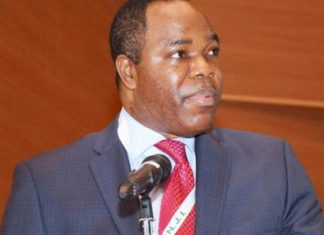 EFCC nabs ex-Skybank chair Tunde Ayeni over alleged N36bn, $30m fraud Man in a navy suit and red tie speaks at a microphone on a stage with a wood-paneled backdrop.
