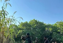 Troops nab 10 terror suspects, rescue 3 victims from kidnappers Soldiers in camouflage gear with rifles stand on a rocky dirt path in a wooded area, a civilian man nearby wearing a black shirt and white sneakers.