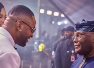 Why I attended BBN’s Cross’ wedding – Atiku Two men greet and smile at an indoor event; one wears a white suit and glasses, the other in traditional blue attire with a head wrap.