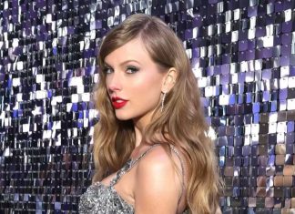 Taylor Swift moves to trademark voice, image after AI concerns Taylor Swift in a shimmering silver sequin gown posing against a reflective sequin backdrop at a glamorous event.