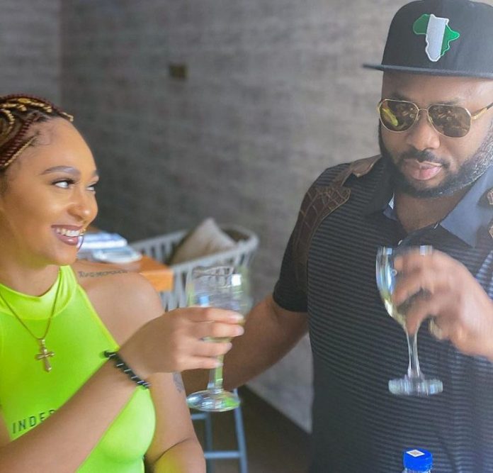Smiling couple toasting with champagne glasses at a casual outdoor gathering, woman in neon green top and man wearing hat and sunglasses.
