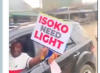 “No Light, No Campaign!” — Edo Youths Protest Ahead of Seyi Tinubu Visit Person leaning out of a car window, holding a sign that reads 'ISOKO NEED LIGHT', likely protesting for electricity.