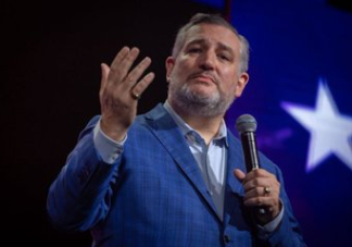 “Government Officials Are Complicit in The Killing of Christians in Nigeria. – Us Senator Ted Cruz Man in a blue suit speaks into a handheld microphone on stage, gesturing with his left hand against a backdrop with a white star.