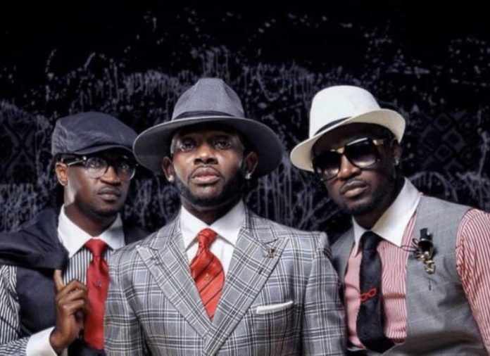 Three men in stylish suits posing for a portrait, wearing hats and sunglasses against a dark backdrop.