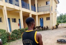 Why I beat female police officers with baton – Suspect Man with a black and yellow basketball jersey (number 23) stands barefoot, facing away outside a yellow building with blue doors.