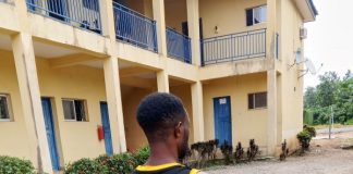 Why I beat female police officers with baton – Suspect Man with a black and yellow basketball jersey (number 23) stands barefoot, facing away outside a yellow building with blue doors.