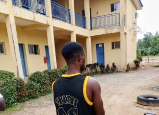 Why I beat female police officers with baton – Suspect Man with a black and yellow basketball jersey (number 23) stands barefoot, facing away outside a yellow building with blue doors.