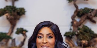 Mo Abudu warns public over fake video promising N700,000 daily earnings Woman in a navy dress smiling softly, resting her chin on her hand, wearing a silver watch and bracelet with a bonsai-filled backdrop behind her.