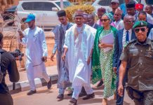 Rep seat: Yusuf Buhari gets automatic APC ticket Group of men in traditional Nigerian attire walking together, escorted by a security officer in front, while a photographer films on a sunny street.