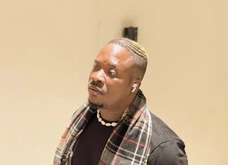 What were you expecting? — Jaywon questions Ilebaye’s father Man wearing a black t‑shirt with a plaid scarf, white shell necklace, and AirPods, looking to the side indoors.
