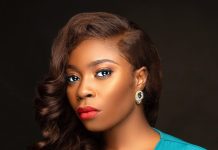 YouTube was never designed for films – Bolaji Ogunmola speaks on filmmaking Portrait of a woman with wavy brown hair, bold makeup (red lips, subtle eye makeup), wearing a teal V-neck dress and a gold earring against a dark backdrop.