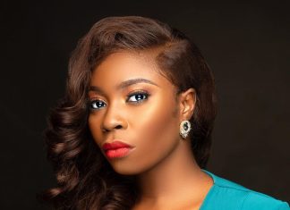 YouTube was never designed for films – Bolaji Ogunmola speaks on filmmaking Portrait of a woman with wavy brown hair, bold makeup (red lips, subtle eye makeup), wearing a teal V-neck dress and a gold earring against a dark backdrop.