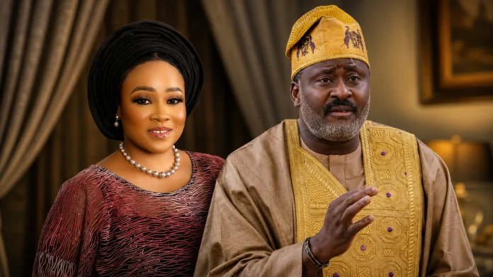 Smiling woman in a black gele and burgundy traditional dress with pearl jewelry, beside a man in gold-embroidered agbada in a warmly lit room.