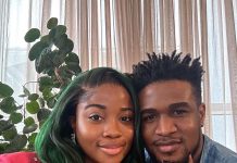 Veekee James, husband welcome baby girl Smiling couple posing for a selfie indoors, with a leafy houseplant in the background and sheer curtains behind them.