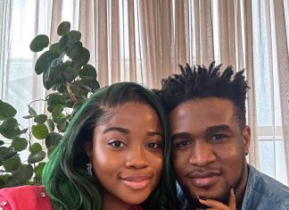 Veekee James, husband welcome baby girl Smiling couple posing for a selfie indoors, with a leafy houseplant in the background and sheer curtains behind them.