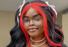 Jarvis threatens to sue Carter Efe over alleged cyberbullying Person with long black hair and bright red highlights, wearing round glasses, pink hair ribbons, and a pearl necklace, smiling at the camera.