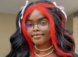 Jarvis threatens to sue Carter Efe over alleged cyberbullying Person with long black hair and bright red highlights, wearing round glasses, pink hair ribbons, and a pearl necklace, smiling at the camera.
