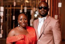 ‘We were going to break up’- Daniel Etim-Effiong opens up on wife’s birthday Couple posing together at a formal event; woman in a red off-shoulder dress, man in a light pink suit and sunglasses.