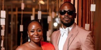 ‘We were going to break up’- Daniel Etim-Effiong opens up on wife’s birthday Couple posing together at a formal event; woman in a red off-shoulder dress, man in a light pink suit and sunglasses.