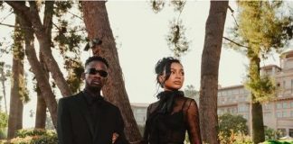 Mr Eazi, Otedola’s daughter Temi, celebrate first wedding anniversary Two individuals in black formal outfits posing on a sunny street framed by trees; man wears a suit with sunglasses, woman in a voluminous black gown.