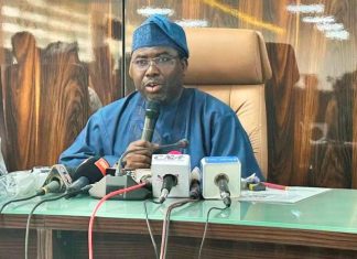 INEC breaks silence on plot to deregister ADC ahead of 2027 Elections Man in blue traditional attire speaking into a handheld mic at a press conference, with several microphones on a glass table in front of him.