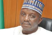 BREAKING: Courts sends ex-Power Minister Mamman to prison for 75 years over ₦33.8bn fraud Portrait of a man wearing a white traditional outfit and a blue patterned cap, seated in a black office chair with a wooden backdrop and a green flag nearby.