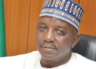 BREAKING: Courts sends ex-Power Minister Mamman to prison for 75 years over ₦33.8bn fraud Portrait of a man wearing a white traditional outfit and a blue patterned cap, seated in a black office chair with a wooden backdrop and a green flag nearby.