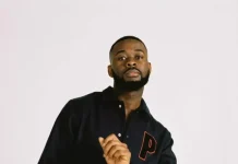 Sarz opens up on how ego affected his career Portrait of a man with a beard wearing a black jacket with a red P patch, looking at the camera.