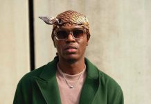Spyro calls out Nigerian pastors over silence amid insecurity Man wearing a patterned headscarf and sunglasses, green overcoat, beige shirt, and a silver necklace, looking at the camera against a neutral background.