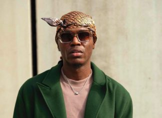 Spyro calls out Nigerian pastors over silence amid insecurity Man wearing a patterned headscarf and sunglasses, green overcoat, beige shirt, and a silver necklace, looking at the camera against a neutral background.
