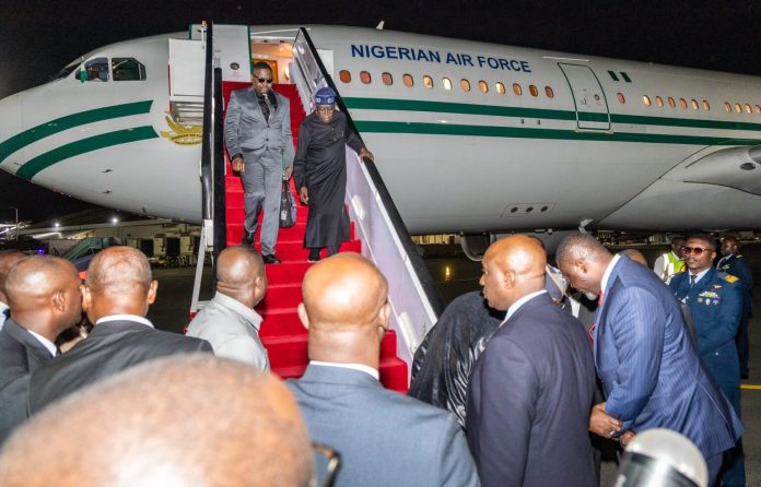 Dignitaries step down from a Nigerian Air Force jet onto a red-carpeted stairs at night, surrounded by officials on tarmac.