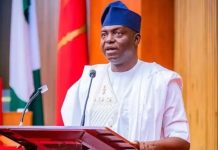 APC disqualifies top House of Reps aspirants from Primaries Man in white traditional attire speaks at a podium with a microphone in a formal setting.