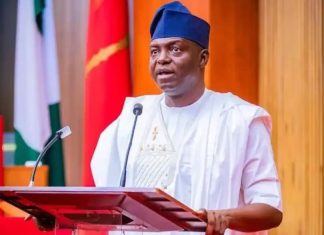 APC disqualifies top House of Reps aspirants from Primaries Man in white traditional attire speaks at a podium with a microphone in a formal setting.
