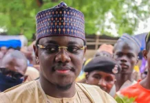 2027: Sule Lamido’s son joins Jigawa governorship race Portrait of a man wearing a patterned traditional cap and glasses at an outdoor gathering.