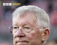 Sir Alex Ferguson Hospitalised After Health Scare at Old Trafford Close-up of an older man with gray hair and glasses, wearing a dark suit and red tie at a sports event (BBC Sport).