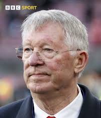 Sir Alex Ferguson Hospitalised After Health Scare at Old Trafford Close-up of an older man with gray hair and glasses, wearing a dark suit and red tie at a sports event (BBC Sport).